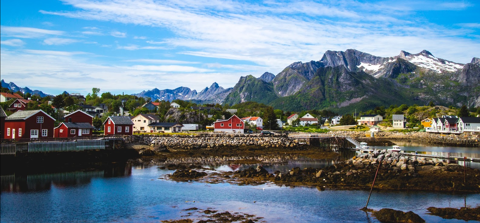 Sea in the foreground, red houses in the middle, and slightly snowy mountains in the background, taken on a sunny day in Kabelvåg from the molo.